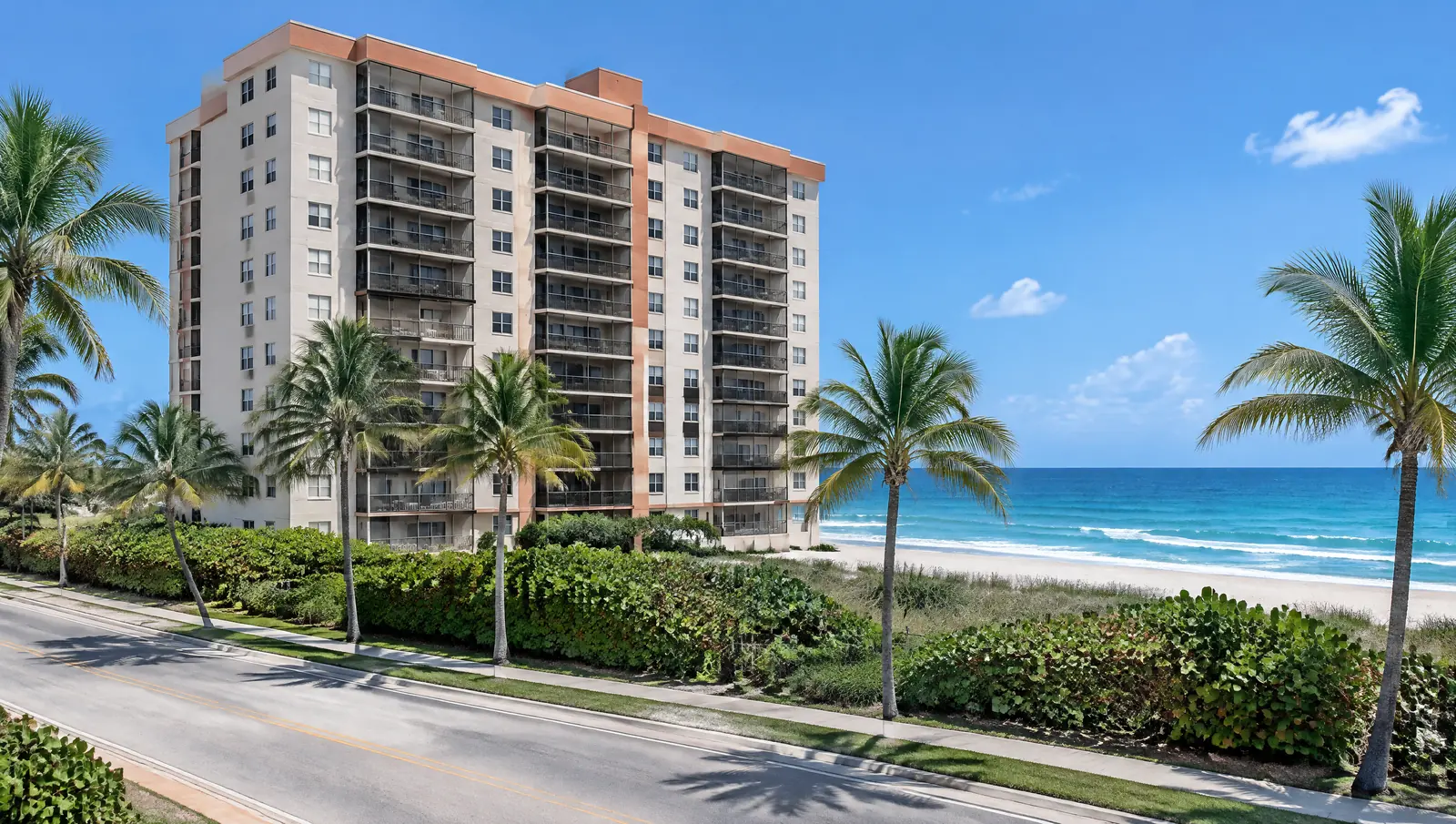 A 1990s ten-storey beachfront condominium behind sea grape and palms on a coastal road