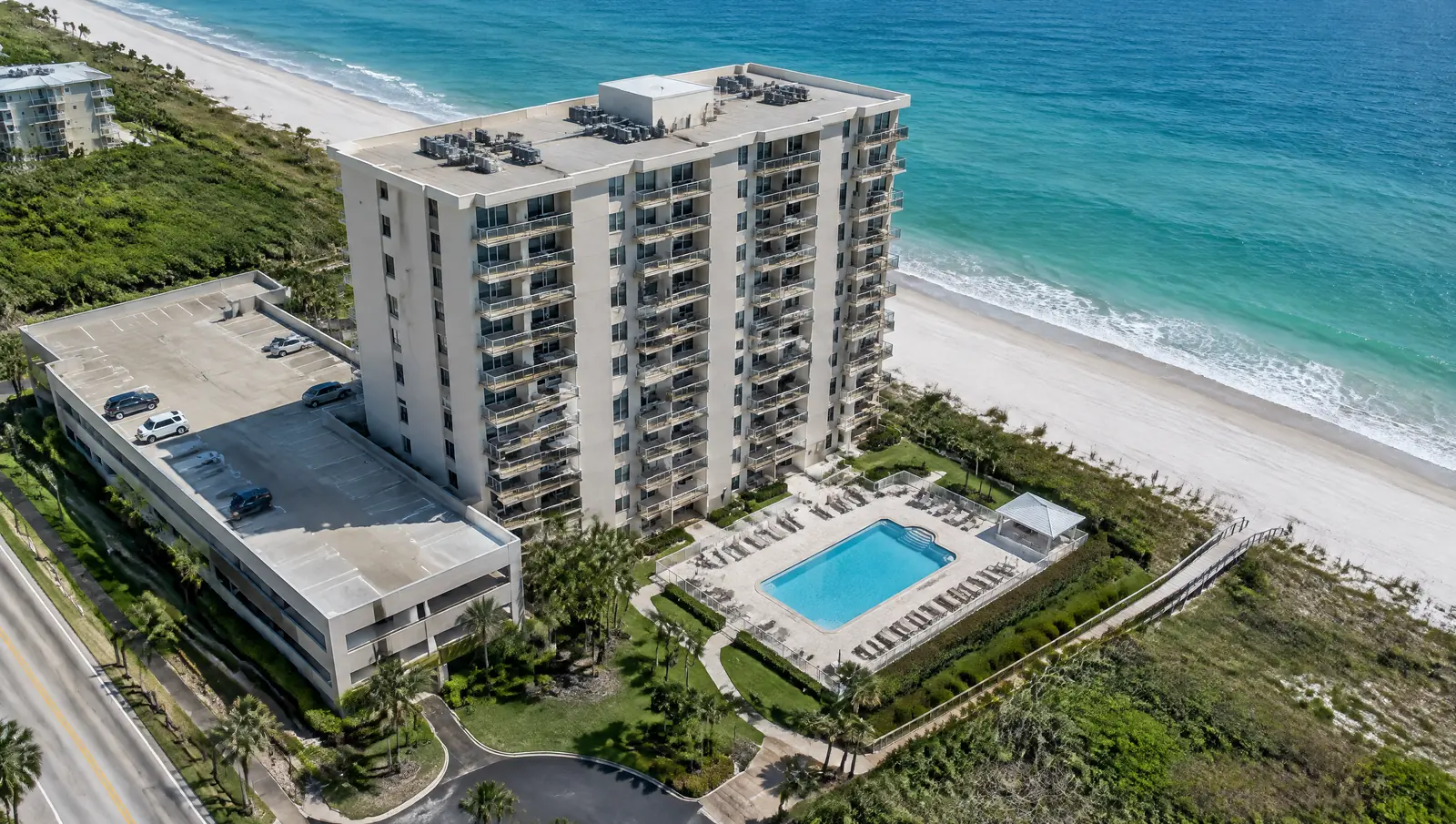 Aerial view of a coastal condominium showing its roof equipment, balconies, pool deck and parking garage