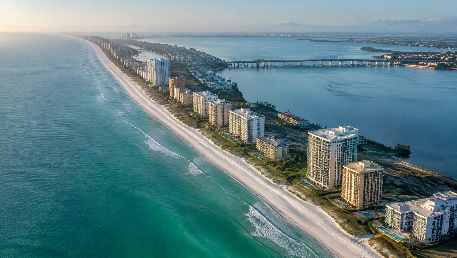 Aerial view of a long Florida barrier island lined with condominium buildings between the Gulf and a bay