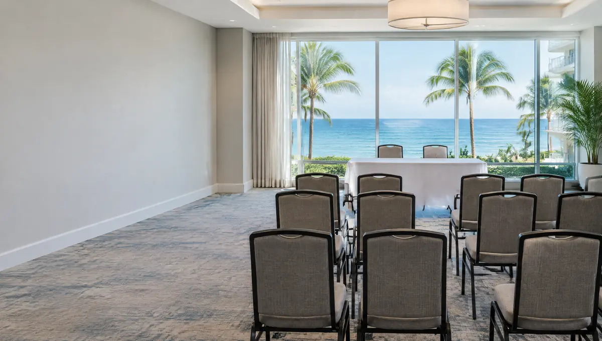 Empty condominium clubroom with rows of chairs facing a table and ocean views through large windows