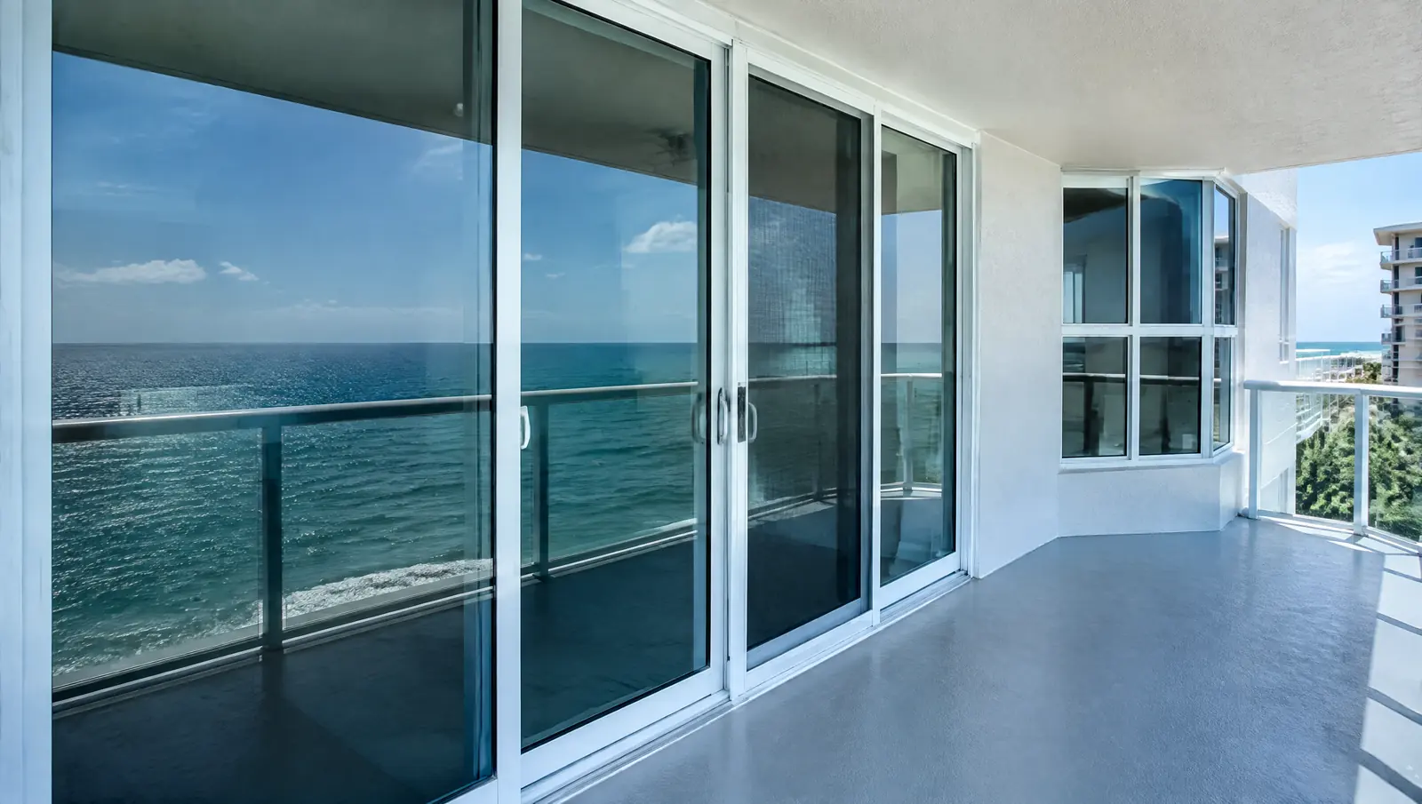 Impact-resistant sliding glass doors and windows opening onto a condo balcony above the ocean
