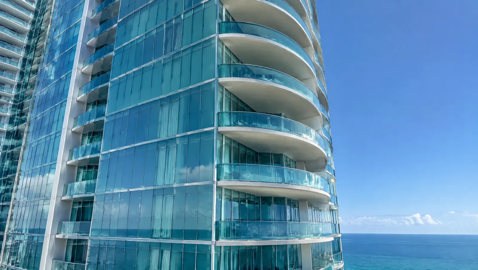 Blue-green glass curtain wall and curved glass balconies of an oceanfront condominium tower